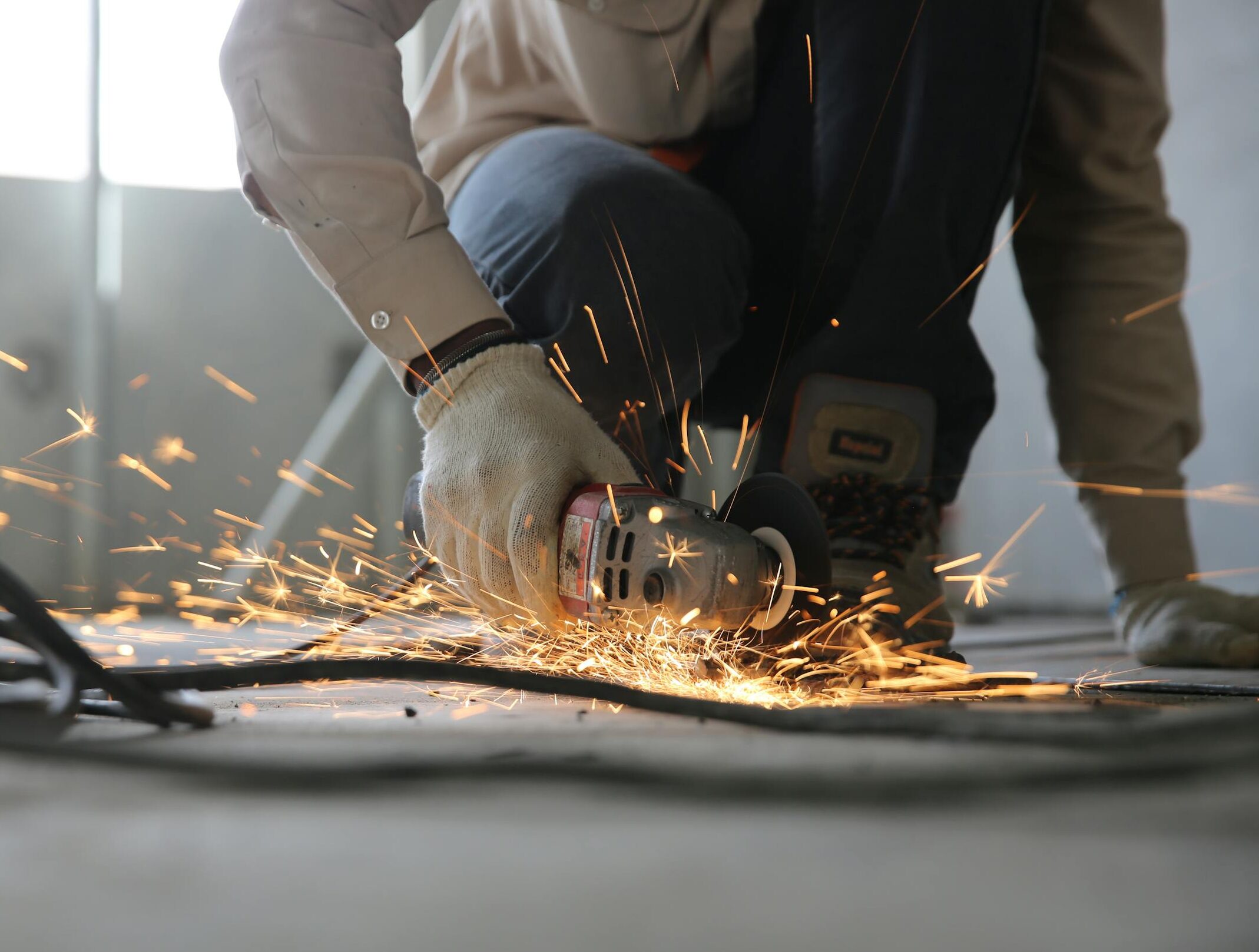 A skilled industrial worker uses a grinder creating a burst of sparks indoors.