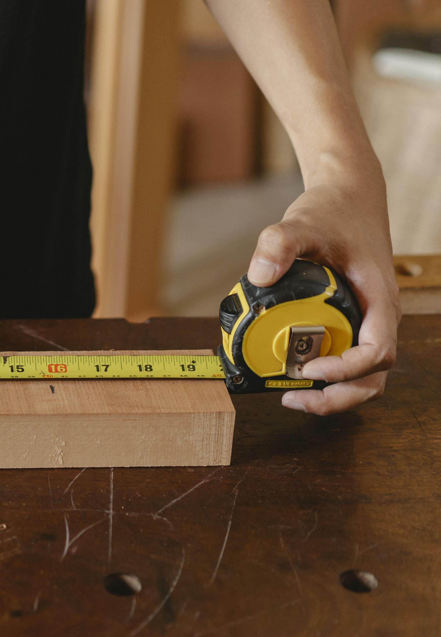 Close-up of carpenter's hand measuring wood with a tape measure in a workshop.
